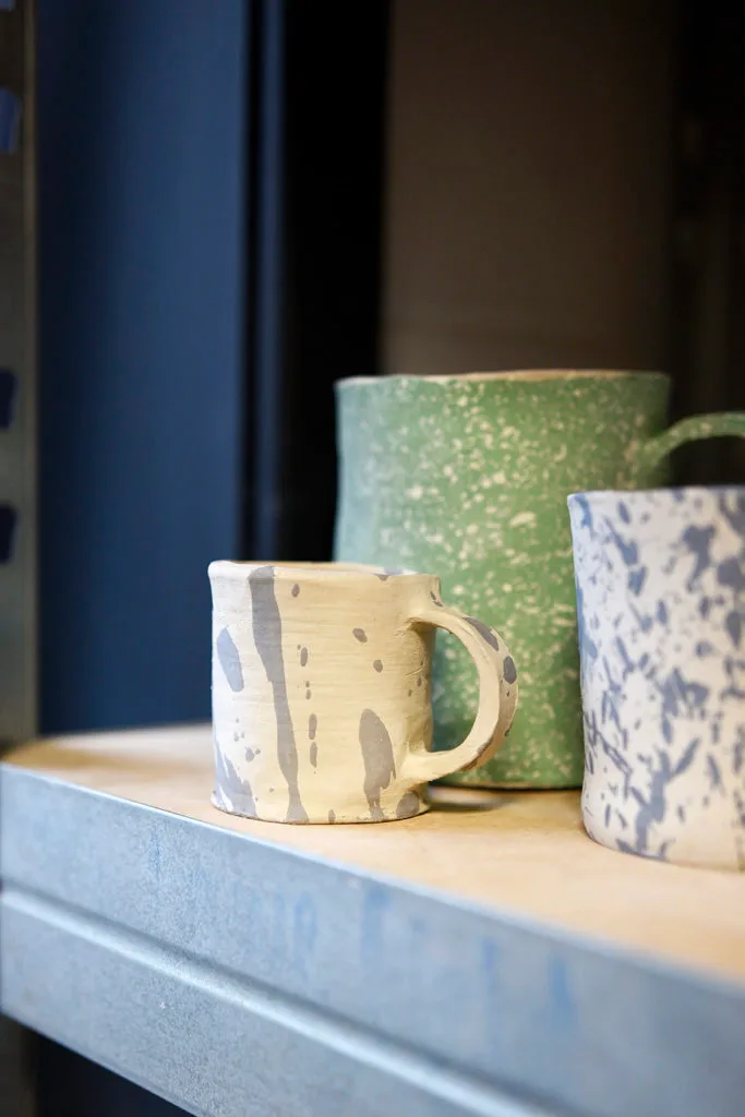 Painted mugs sat on a shelf waiting to go in the kiln.