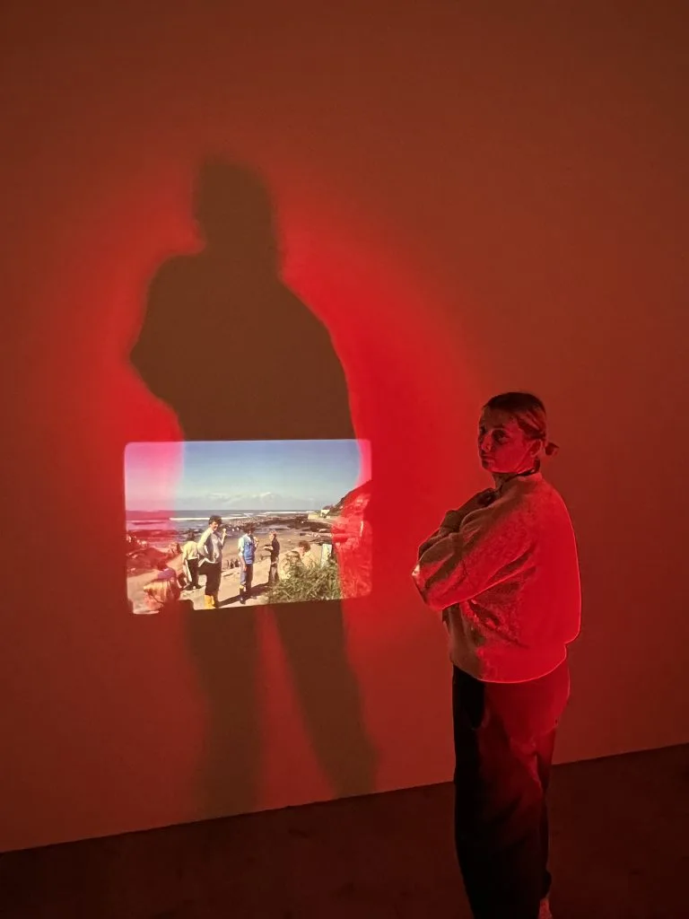 Emma Bentley Fox is stood in a gallery by their artwork.
