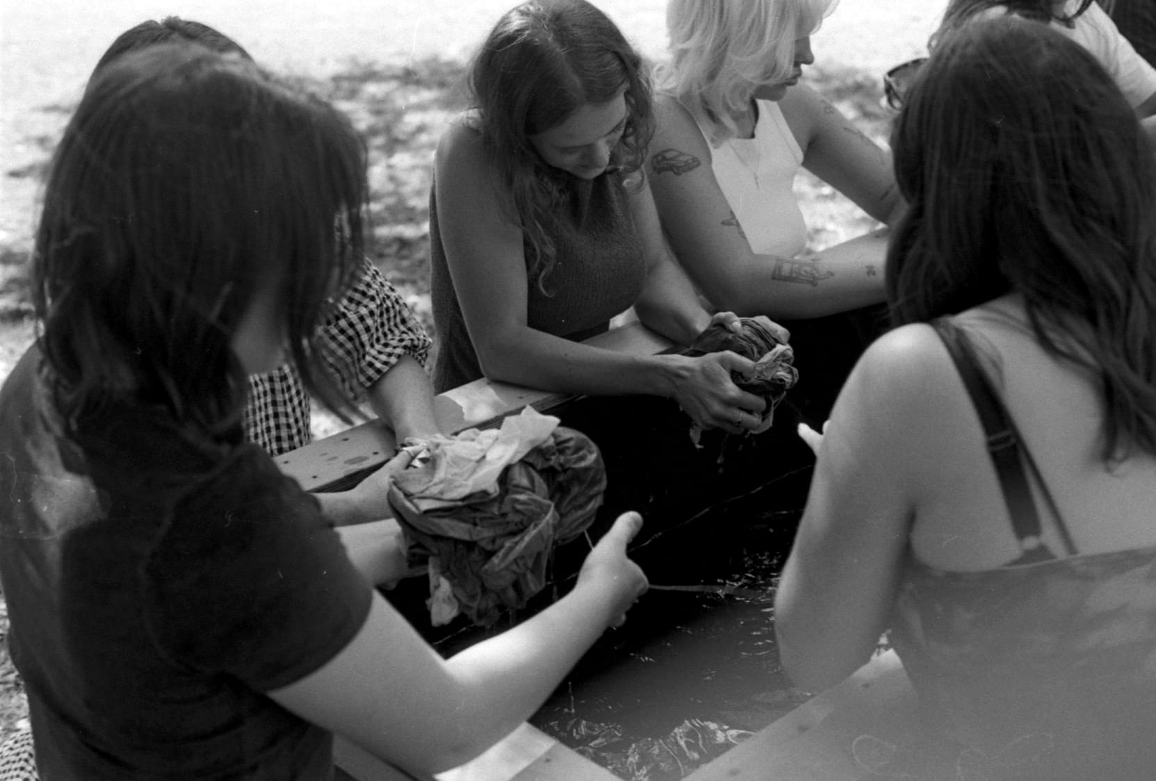 Image from the Divine Archives Exhibition, women are gathered around a trough of water washing cyanotype prints together,