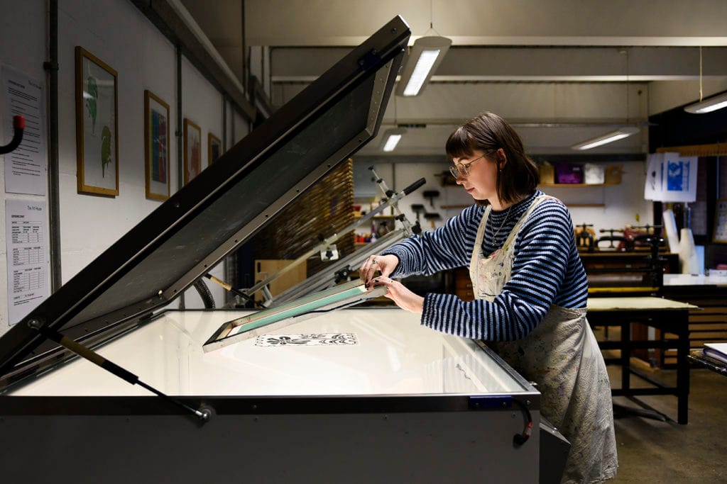 A woman stood at a silk screen exposure unit