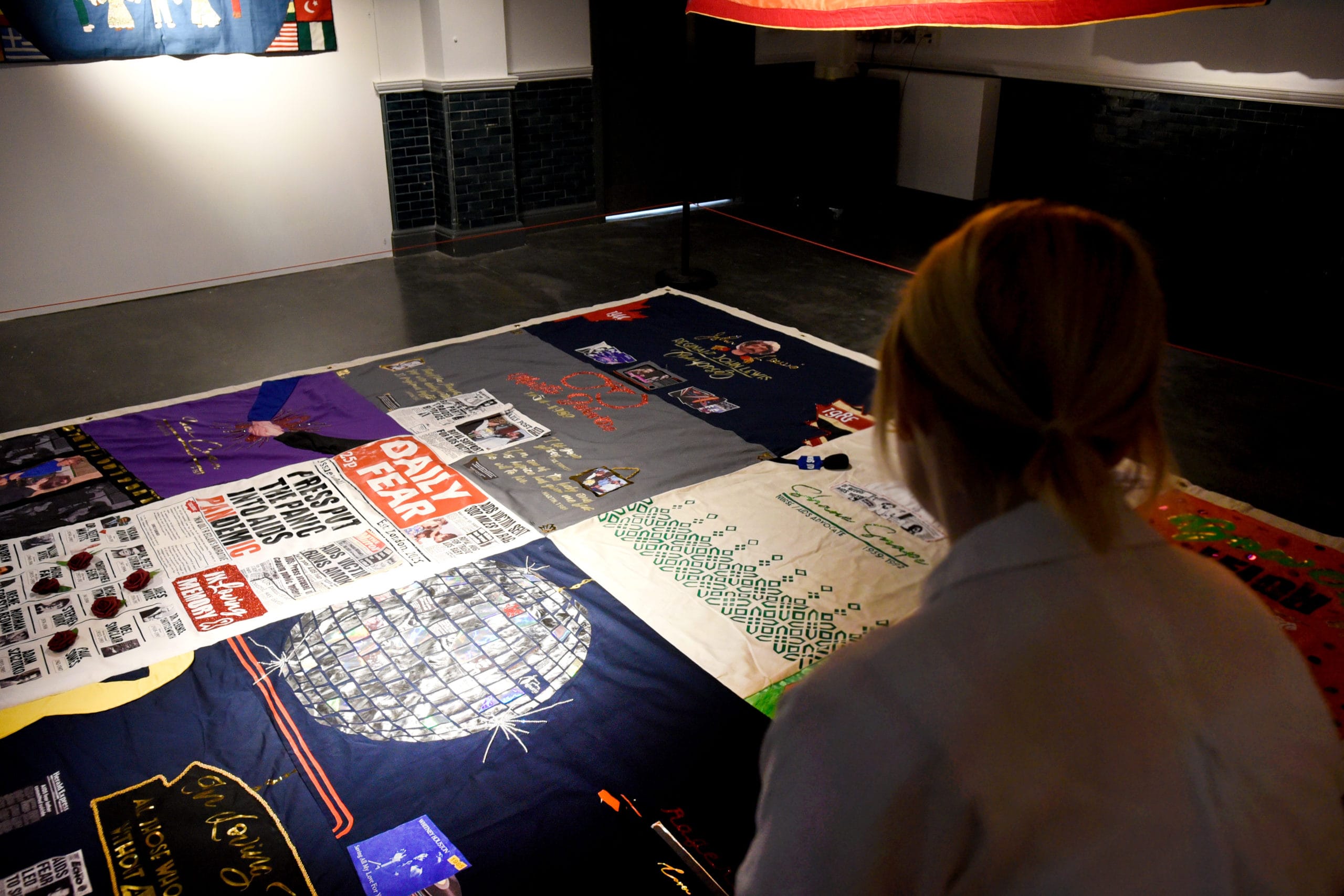 Woman looking at AIDS Memorial Quilt in a darkened gallery